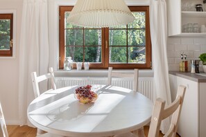 Comedor con mesa redonda, sillas, ventana con vista a vegetación y un radiador debajo.