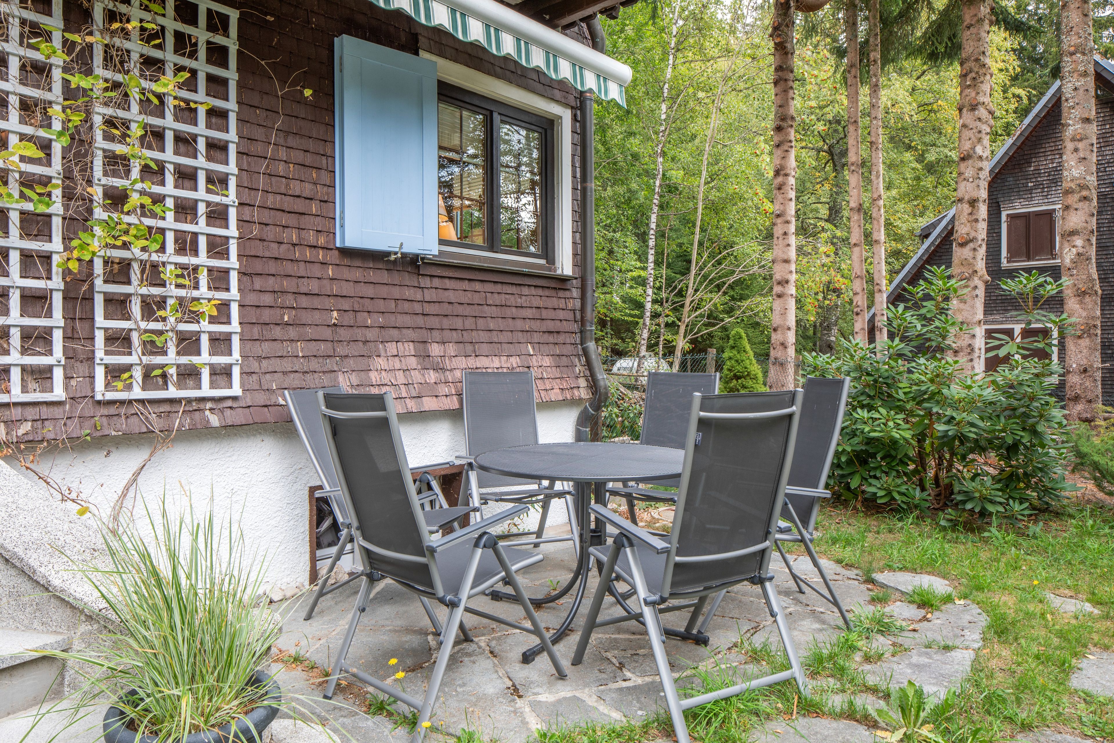 Eine Terrasse mit Tisch und Stühlen, umgeben von einem Garten mit Bäumen und einem Holzzaun.