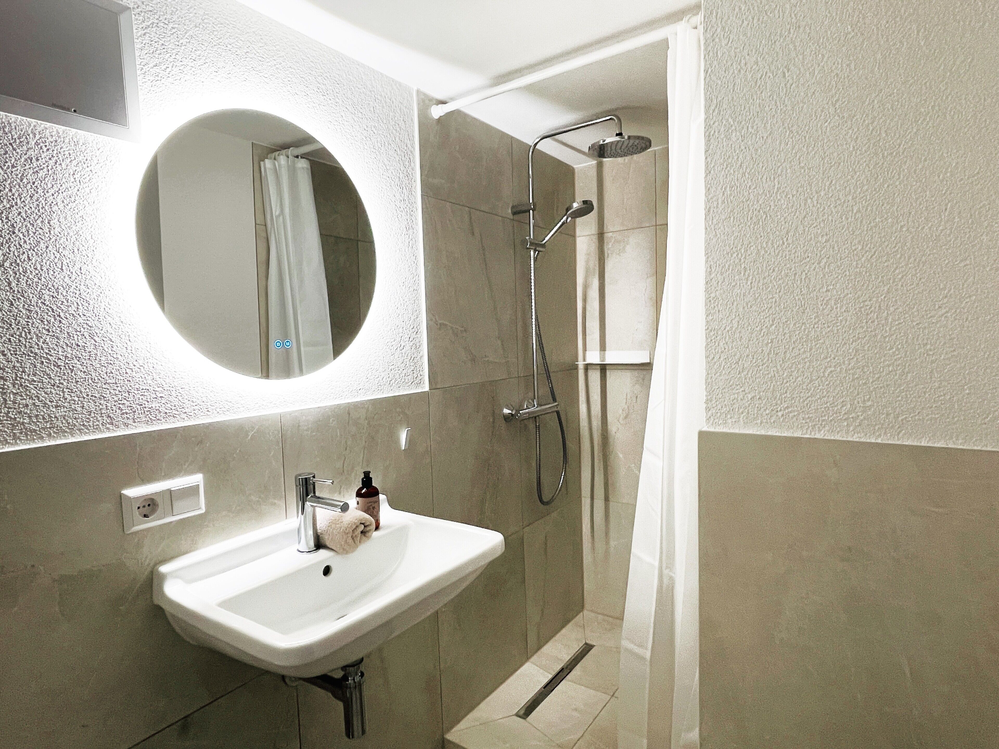Ein Badezimmer mit Waschbecken, Spiegel, Dusche und Handtuch.