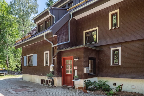 A two-story building with a red door, multiple windows, and a small outdoor seating area.