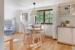 Eine moderne Küche mit weißen Schränken, einem Esstisch mit Stühlen, einer Hängelampe und einem Fenster mit Blick auf Grünflächen.