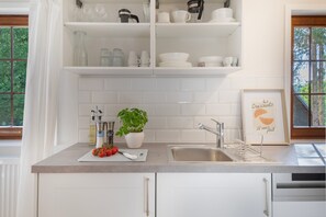 Una cocina con armarios blancos, un lavamanos, una encimera con una planta y un cuadro enmarcado.