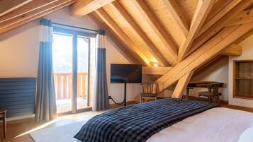 Een slaapkamer met een groot bed, een flatscreen televisie, een houten bureau en een stoel.