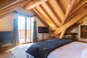 Quarto com uma cama grande, televisão de tela plana, escrivaninha de madeira e uma cadeira.
