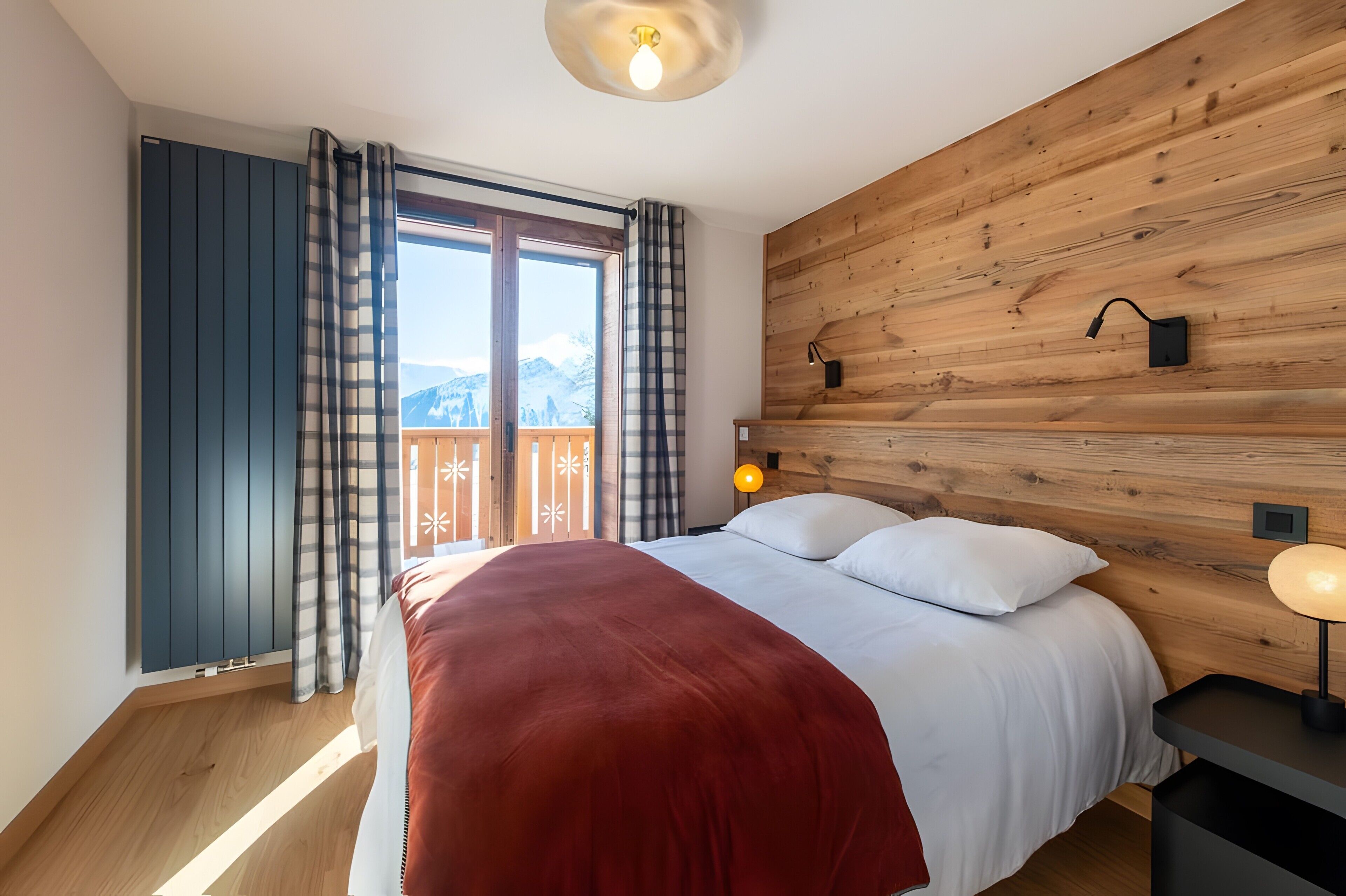 A bedroom with a large bed, wooden headboard, a window with curtains, and a view of mountains.