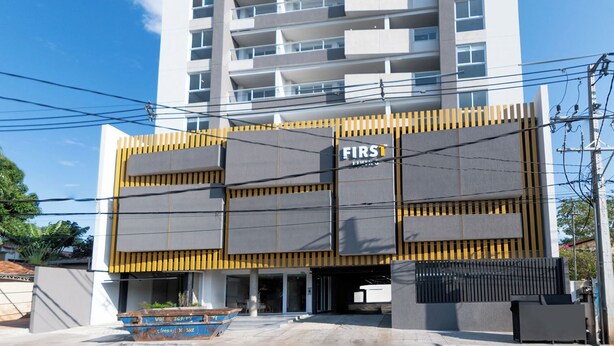 Un edificio de varios pisos con un diseño arquitectónico moderno, destacando una entrada prominente con fachada amarilla y negra.