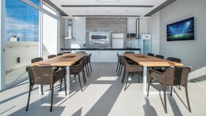 Una cocina moderna con horno empotrado y microondas, un comedor con una mesa grande y sillas, y un ventanal con vistas al cielo.