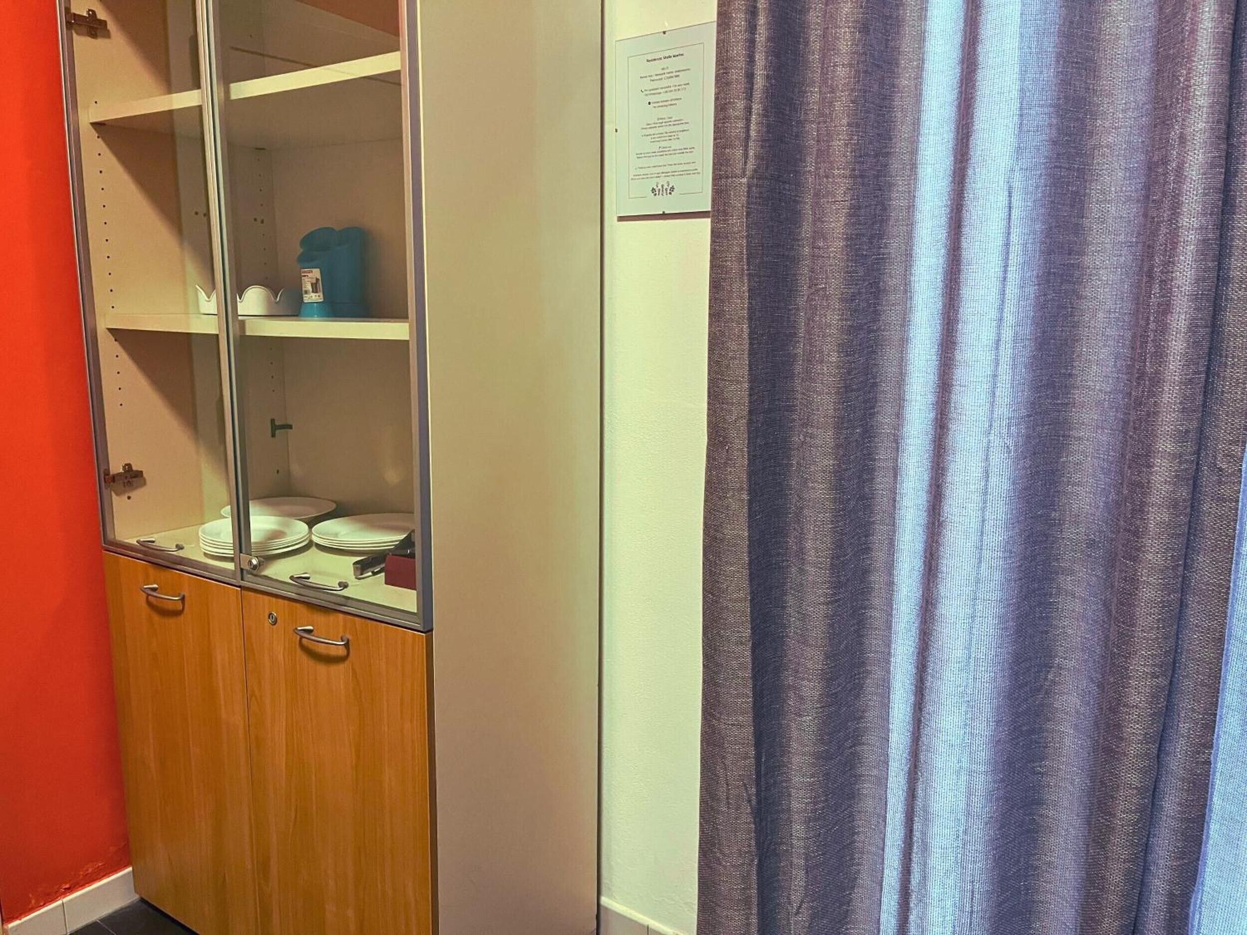 Ein Zimmer mit Holzschrank, einer Glasvitrine mit Geschirr und einem Vorhang.