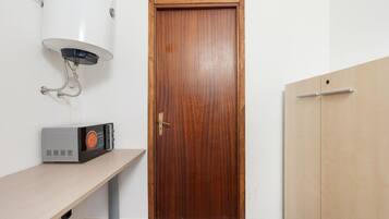 Een kamer met een houten deur, een witte muur, een grijze plank met een zwart apparaat, en een witte wandverwarmers.