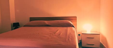 Un lit simple avec une tête de lit en bois, dans une chambre comprenant une table de chevet et une lampe de chevet.