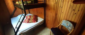 A bunk bed with a mattress and a blanket, a chair with a floral pattern, and wooden walls. - Holiday Home 'La Chaumière Du Tank' with Private Terrace, Private Garden and Wi-Fi (Commes)