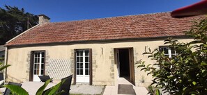 A two-story building with a red-tiled roof, a small porch with a lattice screen, and a door leading to the interior. - Holiday Home 'La Chaumière Du Tank' with Private Terrace, Private Garden and Wi-Fi (Commes)