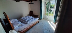 Ein Einzelbett mit Holzrahmen und weißer Bettwäsche in einem Zimmer mit Fliesenboden und Blick durch eine Glastür.
