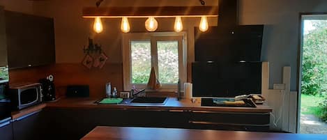 A kitchen with a large island, a microwave, a sink, and a window with a view of greenery.