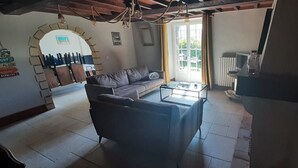 En stue med sofa, sofabord og fjernsyn. Der er et vindue med gardiner, en radiator og en lysekrone.