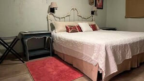 Een slaapkamer met een bed, nachtkastje, rood tapijt, plafondventilator en wandlampen.
