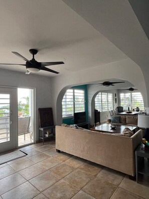 A spacious living area with a ceiling fan, a sofa, a coffee table, and a dining table. - Wind Dancer - Ocean View Retreat (Vieques)