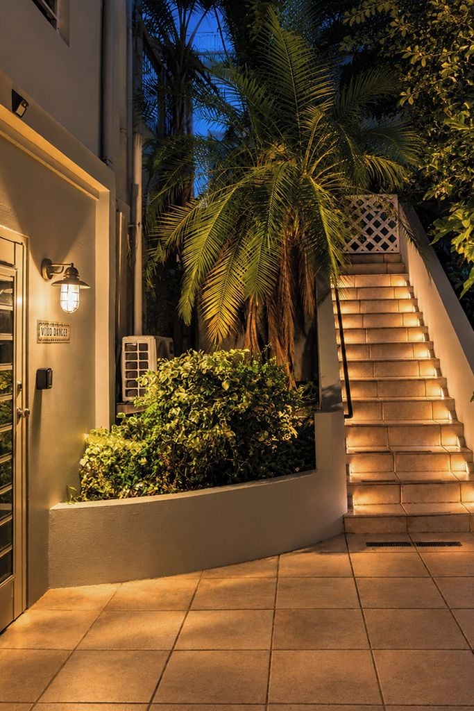 A staircase leading up to a building, surrounded by greenery and a palm tree.
