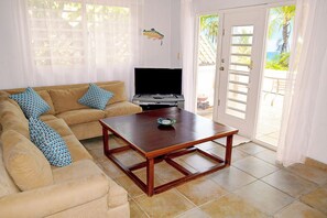A living room with a sofa, a coffee table, a television, and a door leading to a balcony with a view of the sea. - Guesthouse with Panoramic Ocean Views on a quiet street in Vieques (Vieques)