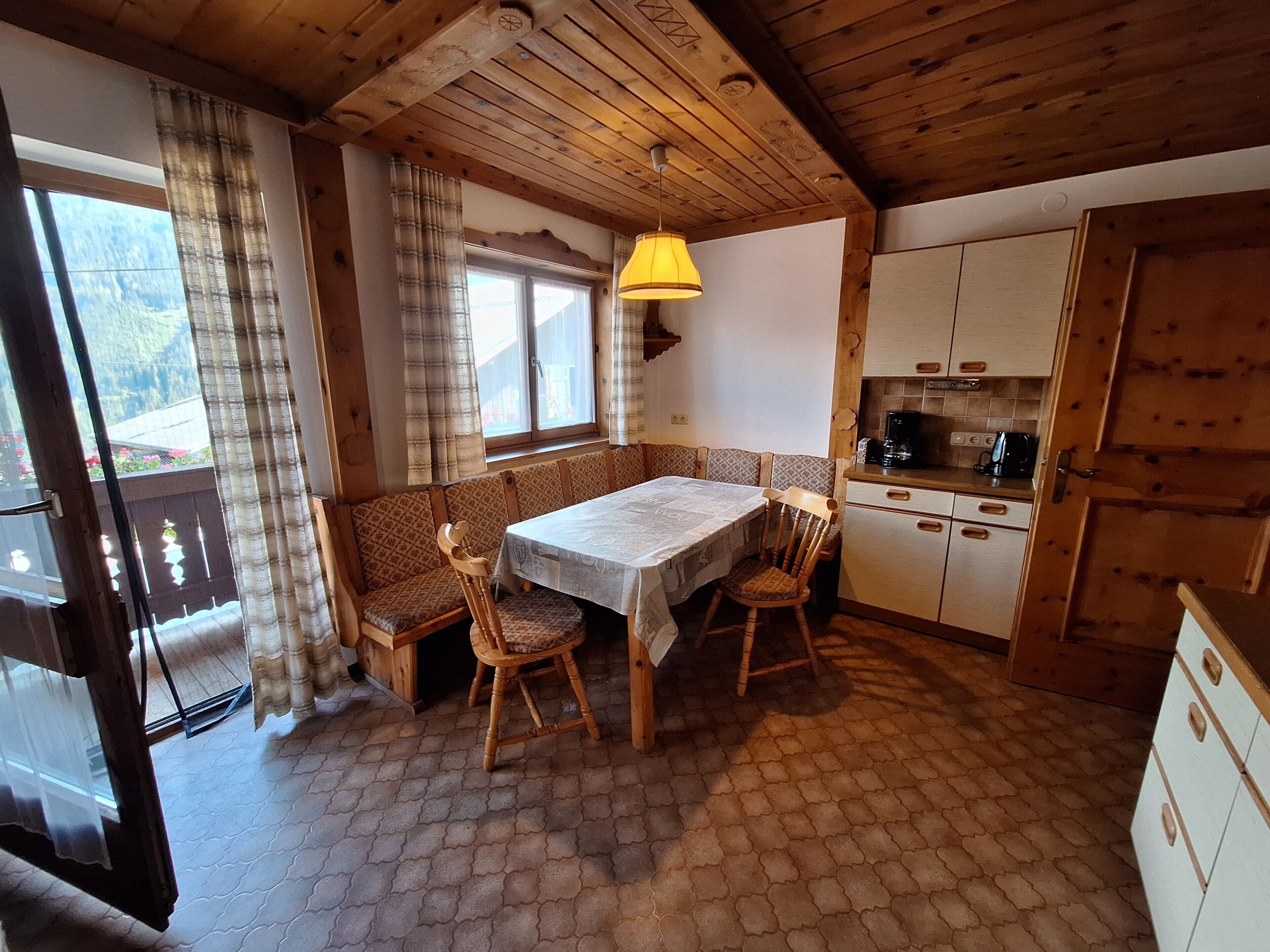 Una cocina acogedora con una mesa y sillas de madera, un banco y una ventana con cortinas.