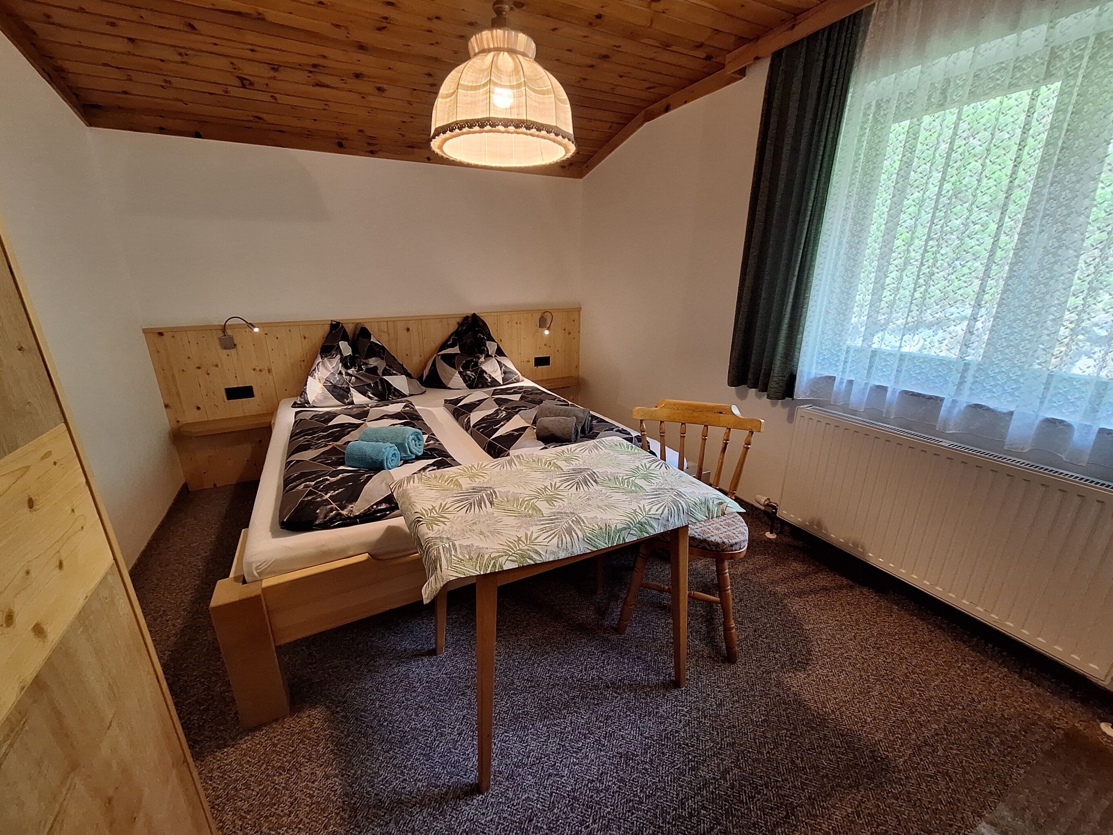 Una habitación de madera con una cama, una silla, una mesa y una ventana con cortinas.