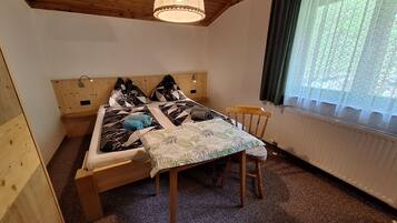 Una habitación de madera con una cama, una silla, una mesa y una ventana con cortinas.