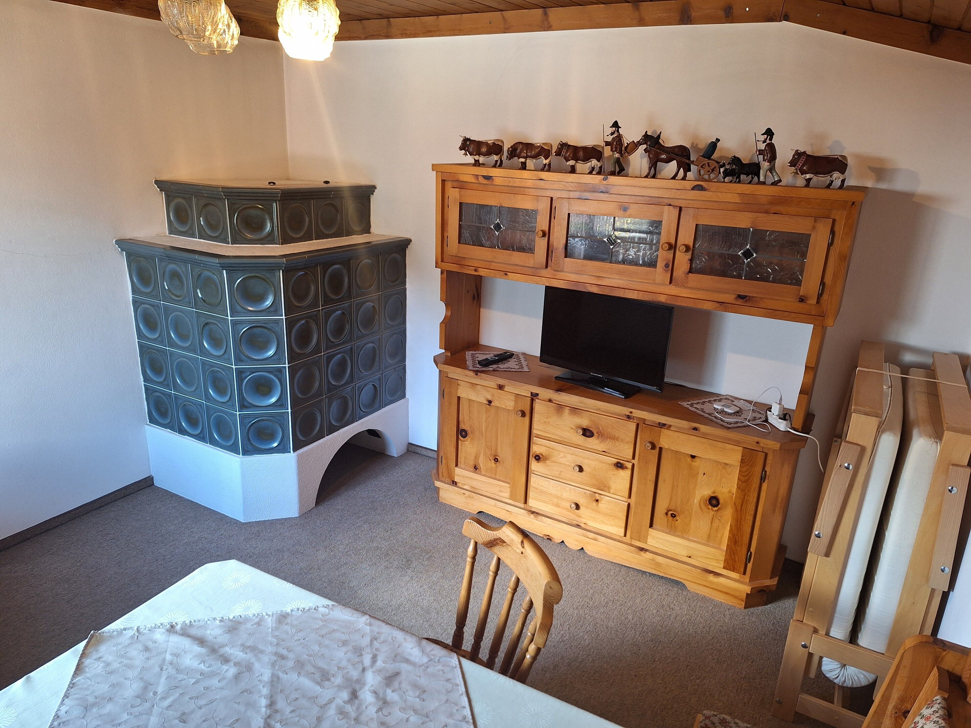 A room with a wooden cabinet with glass doors, a television on top, and a small table with a chair.