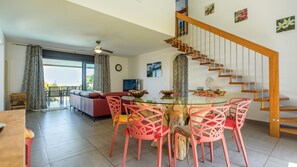 A modern living room with a glass dining table, pink chairs, a red sofa, a staircase, and a balcony with curtains. - Villa “Pay d'Or”: 4-star, sea view, AC, pool, comfort in Saint-Leu (Saint-Leu)