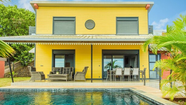 Ein gelbes, zweistöckiges Haus mit Swimmingpool, Gartenmöbeln und einer überdachten Terrasse.