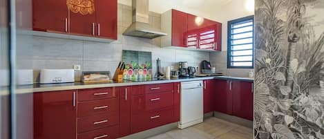 Una cocina moderna con armarios rojos, lavavajillas y una ventana con persianas.