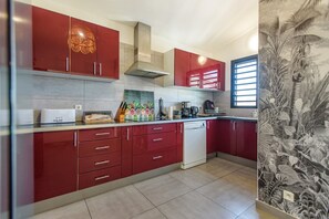 Eine moderne Küche mit roten Schränken, einem Geschirrspüler und einem Fenster mit Jalousien.
