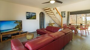 Ein Wohnzimmer mit einem roten Ledersofa, einem Flachbildfernseher, einer Holzeinrichtungsanlage, einem Essbereich mit einem Glastisch und Stühlen sowie einer Treppe mit Holzstufen.