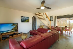 Ein Wohnzimmer mit einem roten Ledersofa, einem Flachbildfernseher, einer Holzeinrichtungsanlage, einem Essbereich mit einem Glastisch und Stühlen sowie einer Treppe mit Holzstufen.