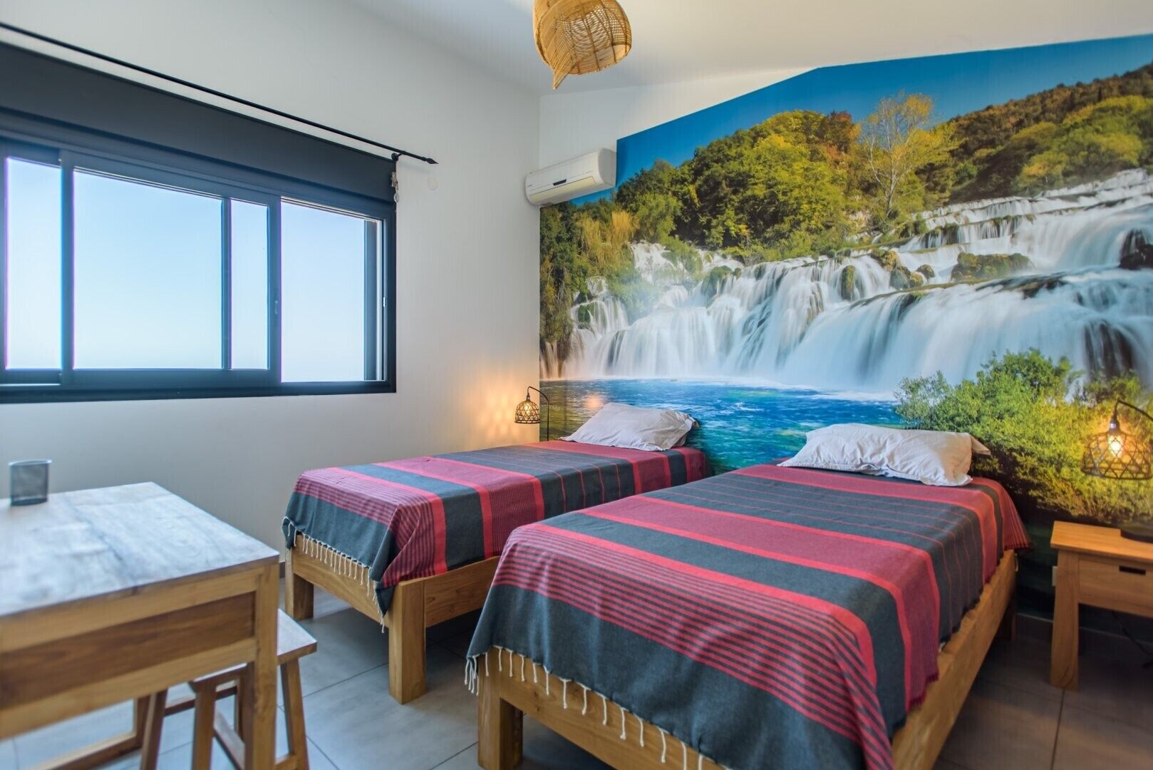 A room with two beds, a desk, and a large mural of a waterfall.
