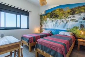 Une chambre avec deux lits, un bureau et une grande fresque représentant une cascade.