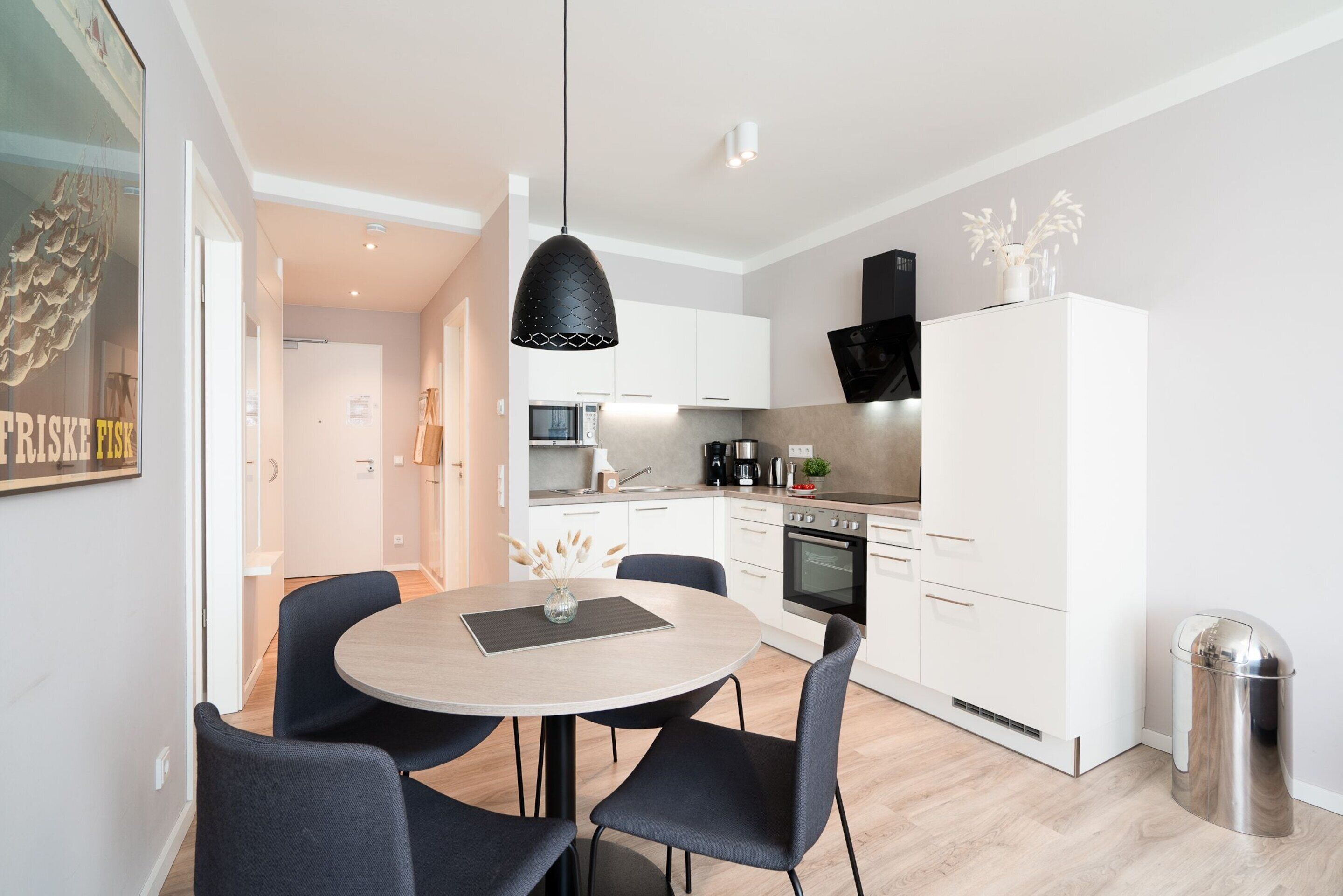 Une cuisine moderne avec des meubles blancs, un four noir et une poubelle en acier inoxydable.