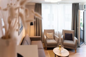 A modern living room with a sofa, two armchairs, a coffee table with a bottle and glasses, and a large window with curtains. - Bright Beach-chair Baltic Suite (Lübeck)