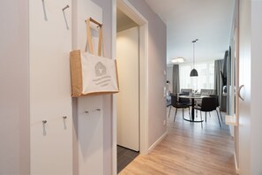 En gang der fører til et spiseområde med et bord og stole, en hængende lampe og en dør med en taske hængende på.