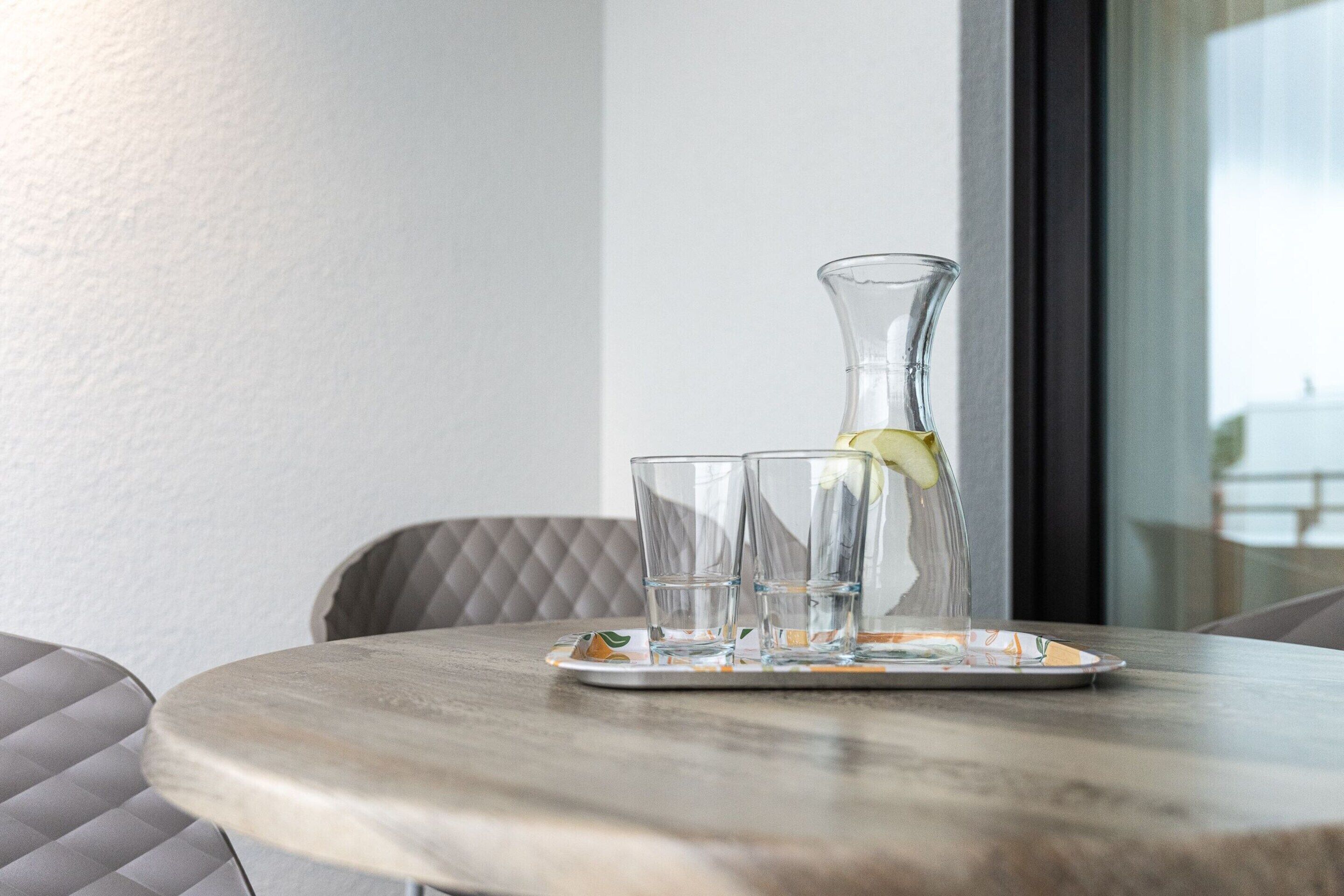 Una mesa con una jarra de vidrio y dos vasos sobre un posavasos.