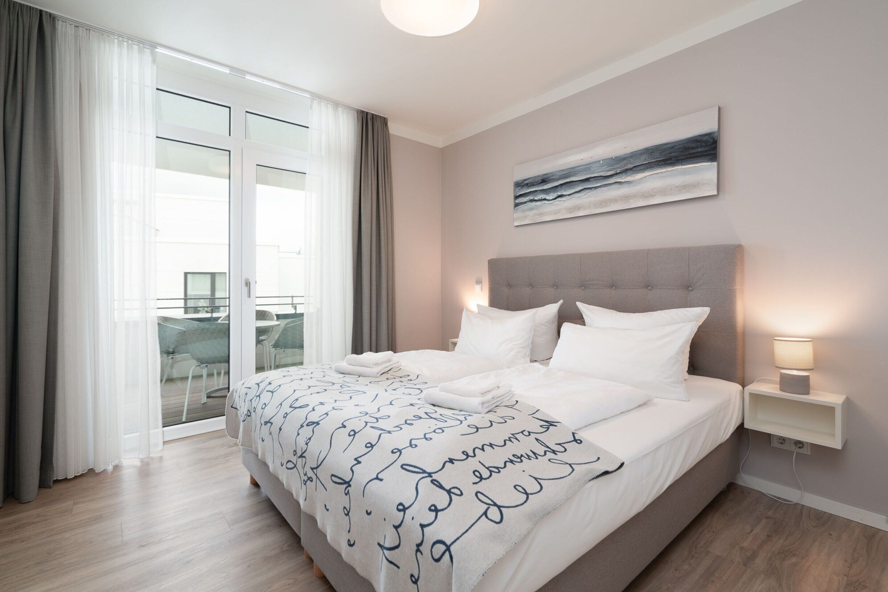 Un dormitorio moderno con una cama grande, vistas al exterior a través de una puerta corredera y un cuadro en la pared.