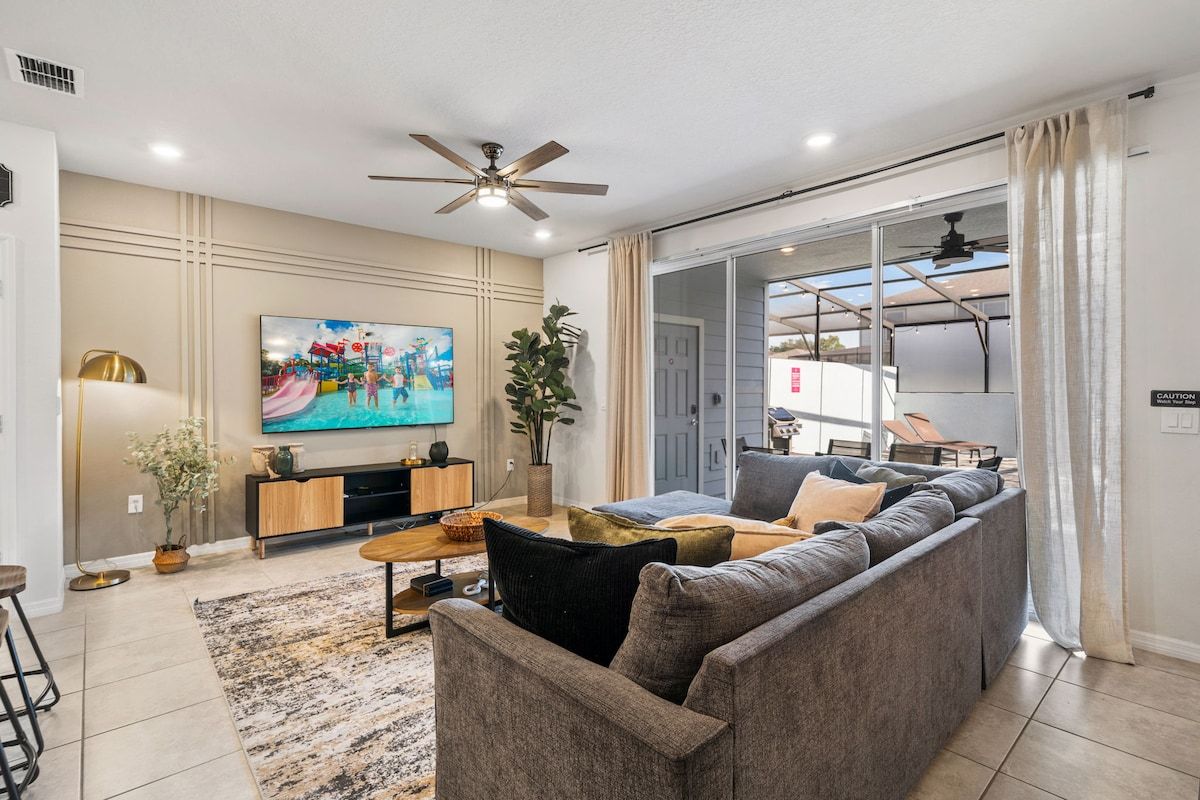 A modern living room with a grey sofa, a coffee table, and a flat-screen TV mounted on the wall.