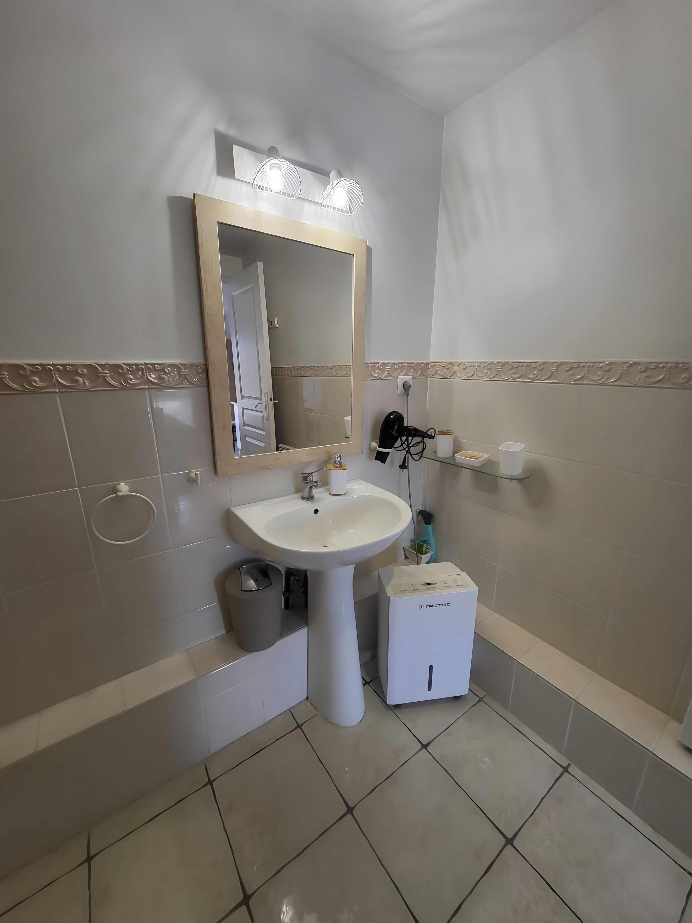 Un baño con lavamanos, espejo, toallero y un pequeño armario blanco.