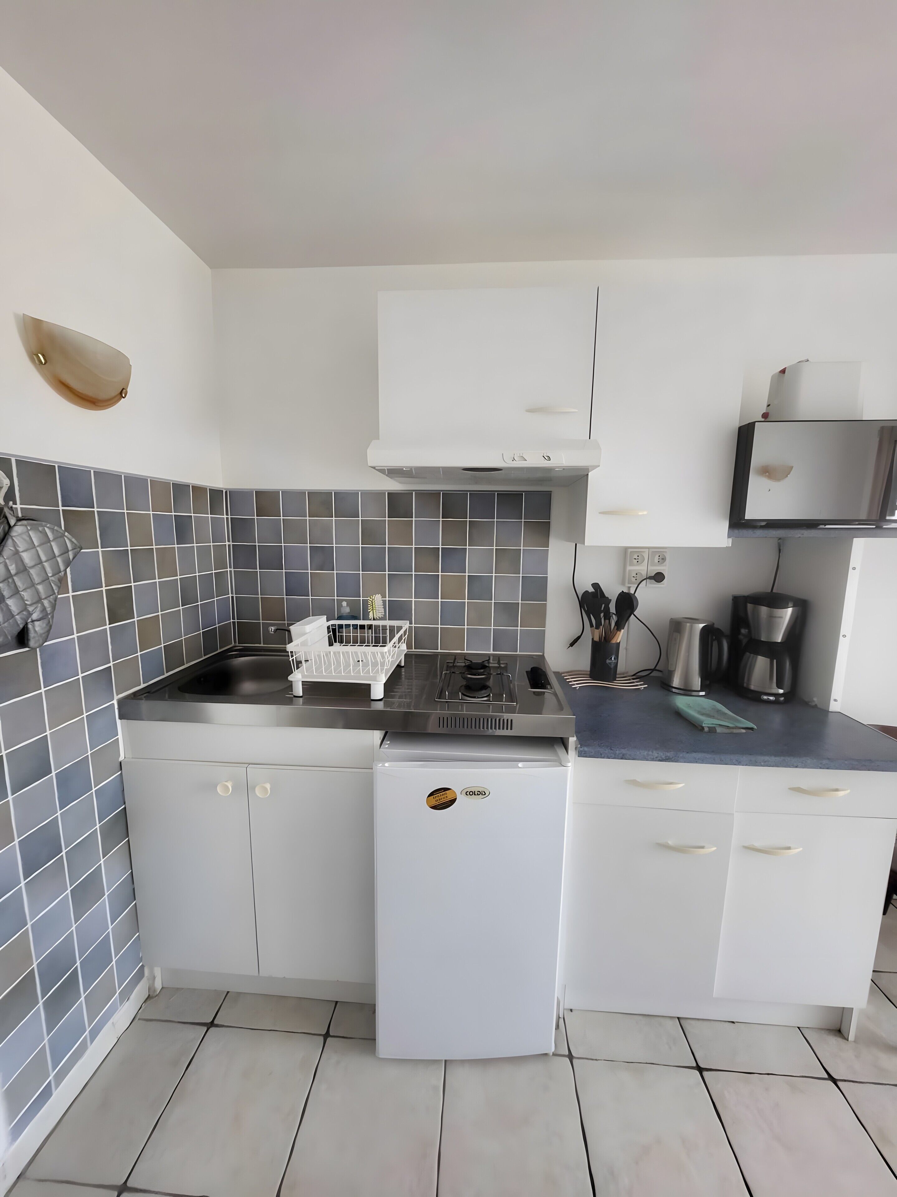 Una cocina compacta con estufa a gas, refrigerador blanco y cafetera.