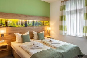 A hotel room with a bed, two bedside tables, a headboard with a forest mural, and a window with curtains. - Studio Apartment 'Haus Kuhlmann' with Shared Garden and Wi-Fi (Landkreis Goslar)