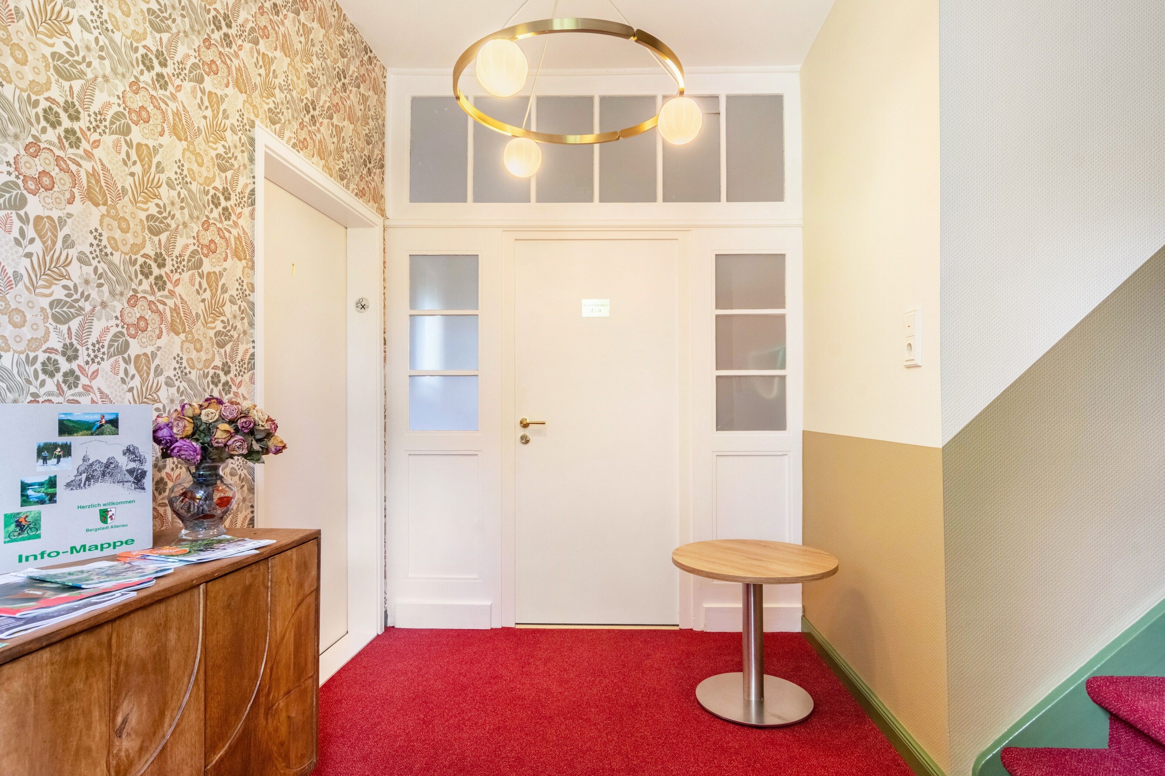 A hotel reception area with a wooden desk, a small round table, and a wall-mounted light fixture.