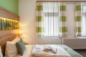 A hotel room with a bed, a painting on the wall, a lamp, and two windows with curtains. - Studio Apartment 'Haus Kuhlmann' with Shared Garden and Wi-Fi (Landkreis Goslar)