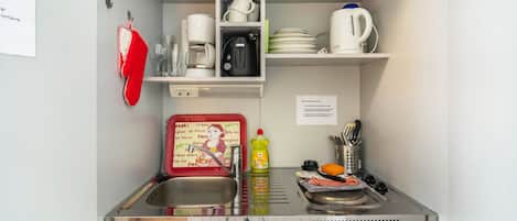 Une petite cuisine équipée d’un évier, d’une machine à café, d’une bouilloire et de divers ustensiles de cuisine.