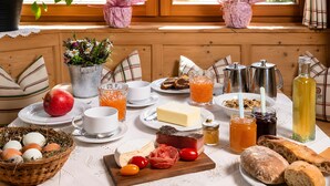 A breakfast setting with a variety of food items, a coffee pot, and a bottle of juice on a table by a window with plants. - Apartment 'Binterhof Rosalpina Bio' with Mountain View, Balcony and Wi-Fi (Kastelruth)