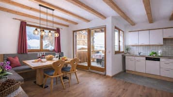 A cozy kitchen with wooden beams, a dining area with a table and chairs, and a view of a snowy landscape through the windows.
