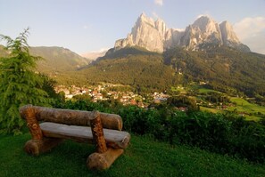 A wooden bench overlooking a village with a mountain range in the background. - Apartment 'Binterhof Rosalpina Bio' with Mountain View, Balcony and Wi-Fi (Kastelruth)